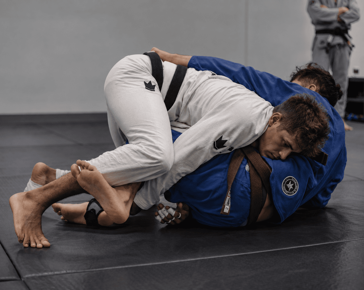 Two students rolling on the mats — white gi passing the guard of a blue gi